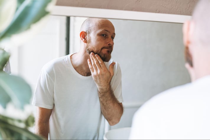 bearded man examines face in the mirror