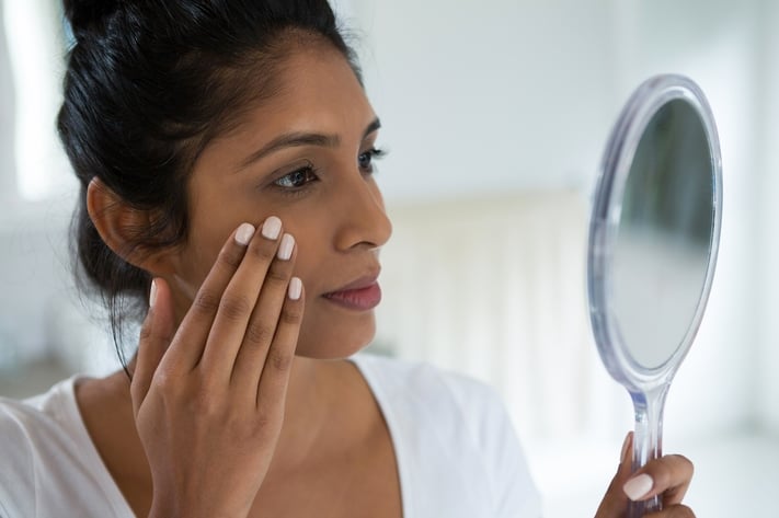 woman examining skin in the mirror