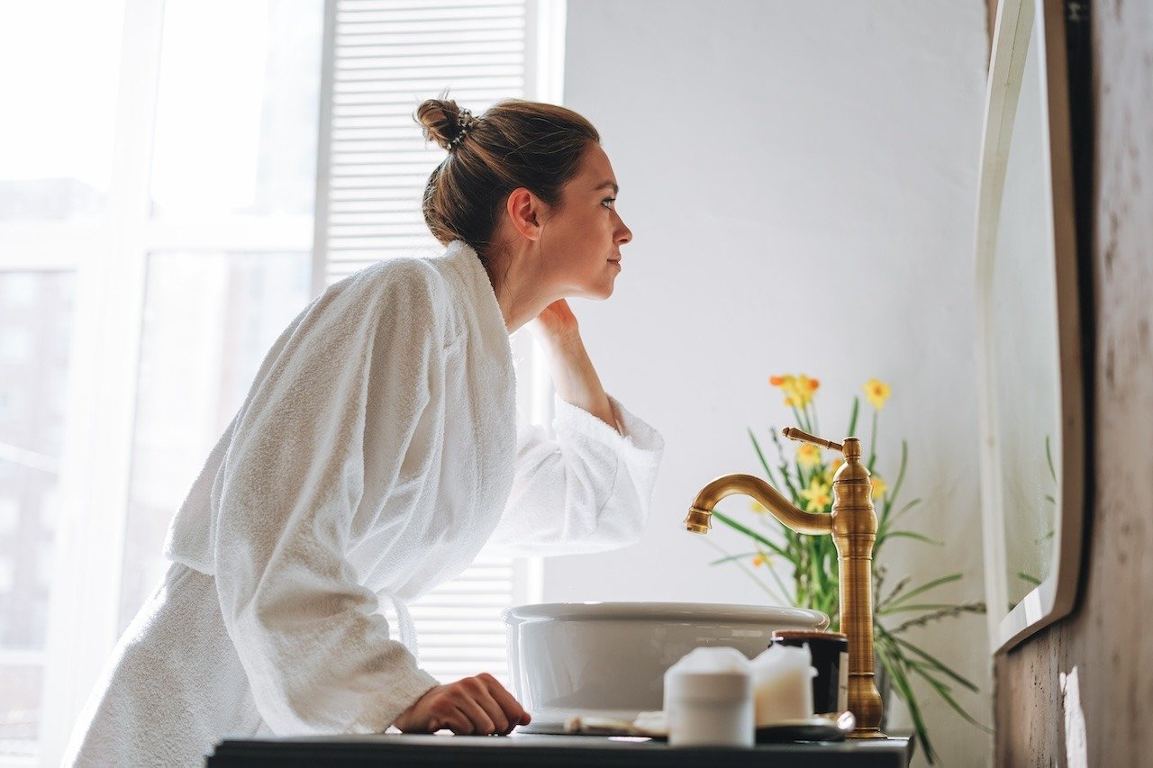 woman looking at skin in the mirror