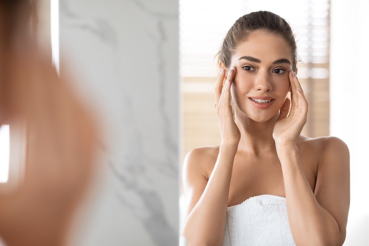 woman looking at skin in the mirror