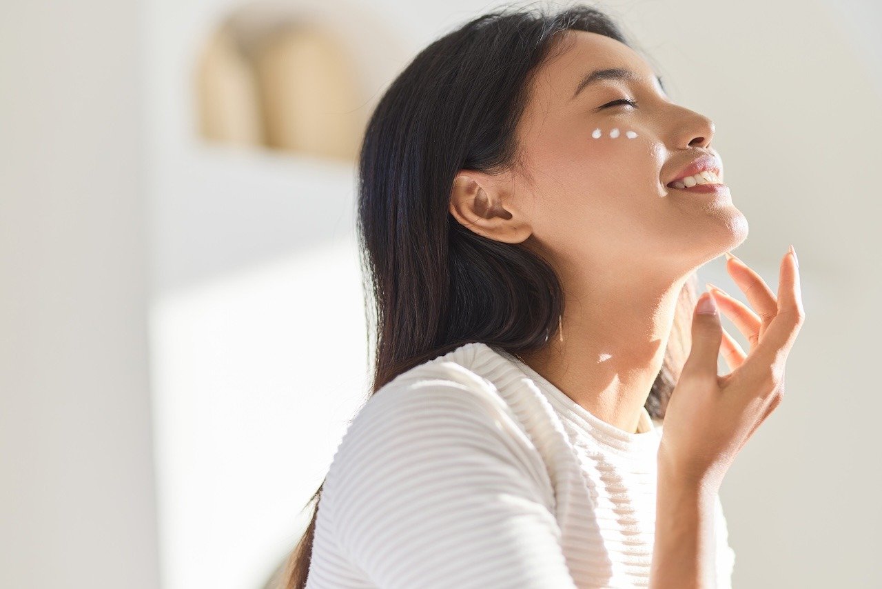 happy young woman applying moisturizer