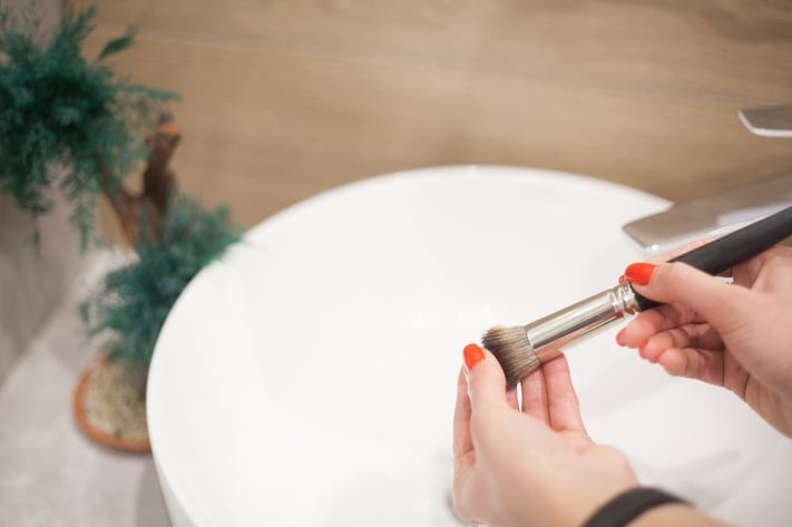 woman washing makeup brush to avoid clogged pores