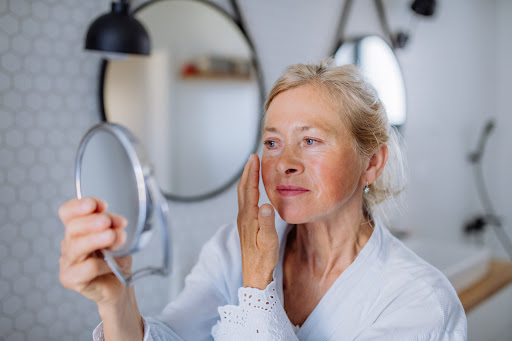 woman liking in the mirror and applying moisturizer to face
